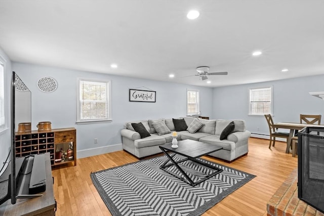 living room featuring ceiling fan, a baseboard radiator, light hardwood / wood-style flooring, and a wealth of natural light