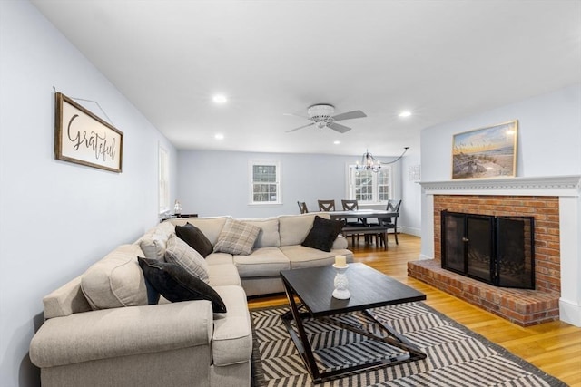 living room featuring a brick fireplace, ceiling fan with notable chandelier, and light hardwood / wood-style flooring