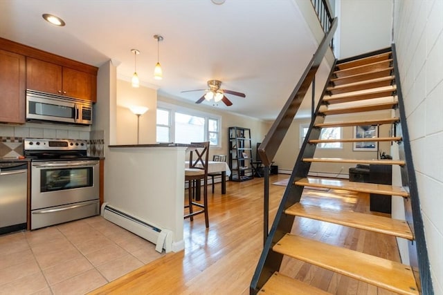 stairs with baseboard heating, ornamental molding, ceiling fan, and wood finished floors