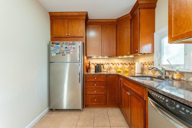 kitchen with brown cabinets, a sink, backsplash, dark stone counters, and appliances with stainless steel finishes