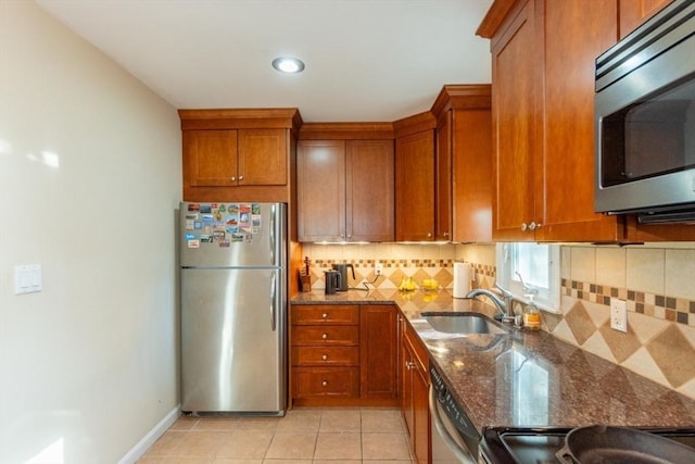 kitchen featuring dark stone countertops, brown cabinetry, a sink, appliances with stainless steel finishes, and backsplash