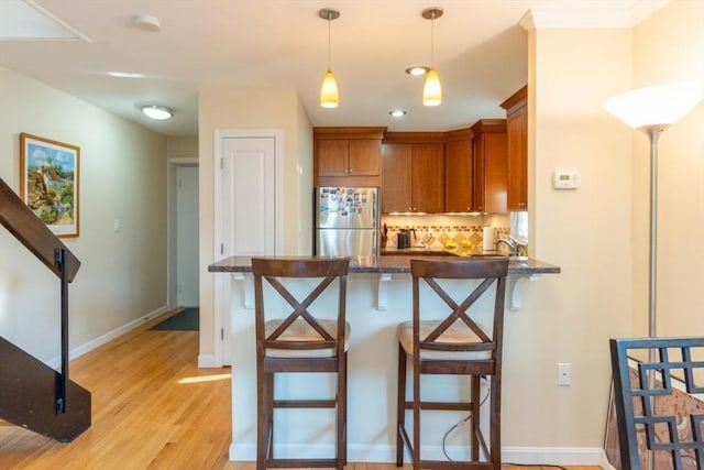 kitchen featuring light wood-type flooring, tasteful backsplash, freestanding refrigerator, a peninsula, and brown cabinetry