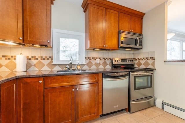 kitchen with brown cabinetry, a baseboard radiator, appliances with stainless steel finishes, light tile patterned flooring, and a sink