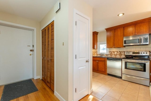 kitchen with brown cabinetry, a sink, appliances with stainless steel finishes, dark countertops, and backsplash