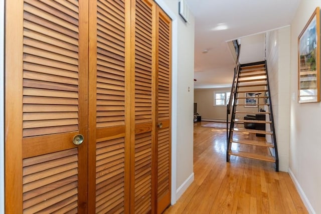 hall with light wood-style flooring, stairs, and baseboards