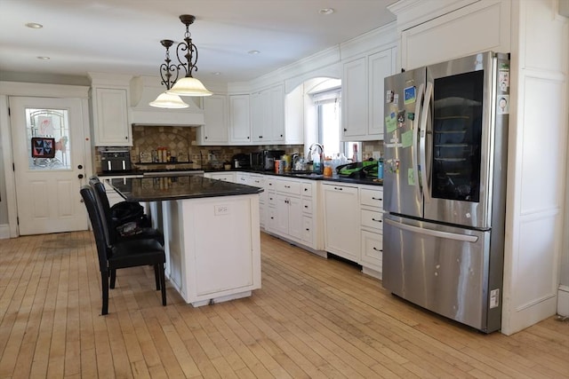 kitchen with stainless steel refrigerator, white cabinetry, hanging light fixtures, and a kitchen island