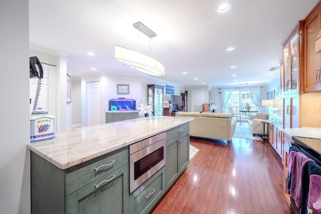 kitchen featuring stainless steel microwave, dark hardwood / wood-style flooring, hanging light fixtures, light stone counters, and crown molding