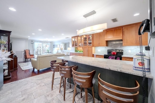 kitchen with a breakfast bar area, decorative light fixtures, electric range, light stone countertops, and decorative backsplash