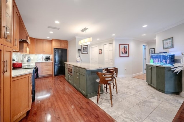 kitchen featuring light stone counters, crown molding, decorative light fixtures, a center island, and black appliances