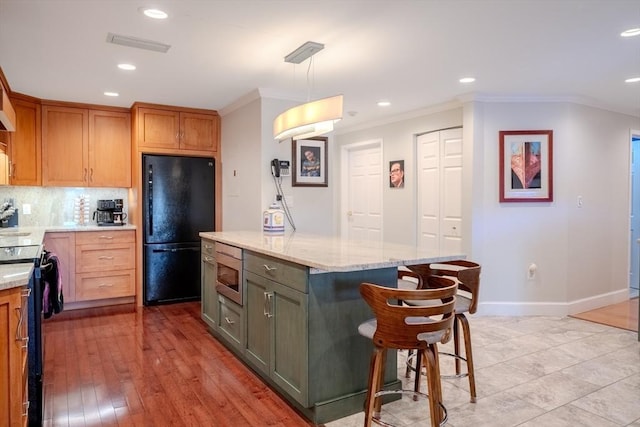 kitchen featuring tasteful backsplash, hanging light fixtures, a center island, light stone counters, and black appliances