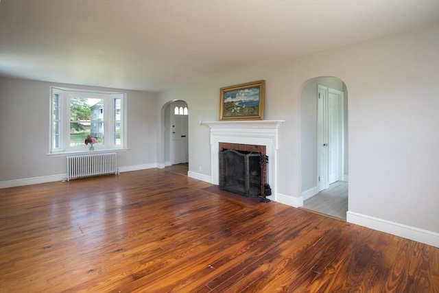 329 Read St, Somerset, MA 02726 - unfurnished living room featuring radiator, arched walkways, a brick fireplace, and wood finished floors