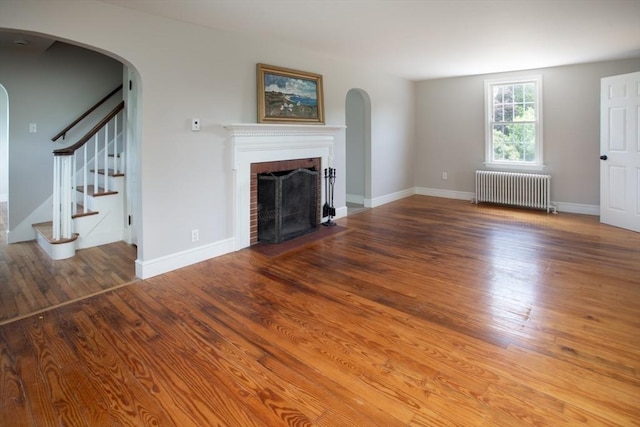 329 Read St, Somerset, MA 02726 - unfurnished living room with radiator, arched walkways, a fireplace, and wood finished floors