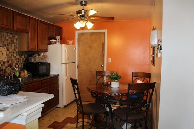 kitchen featuring a ceiling fan, backsplash, freestanding refrigerator, black microwave, and a sink