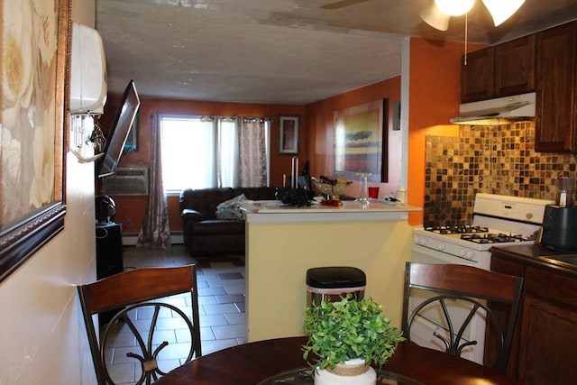 kitchen with ceiling fan, under cabinet range hood, tile patterned floors, tasteful backsplash, and white gas range