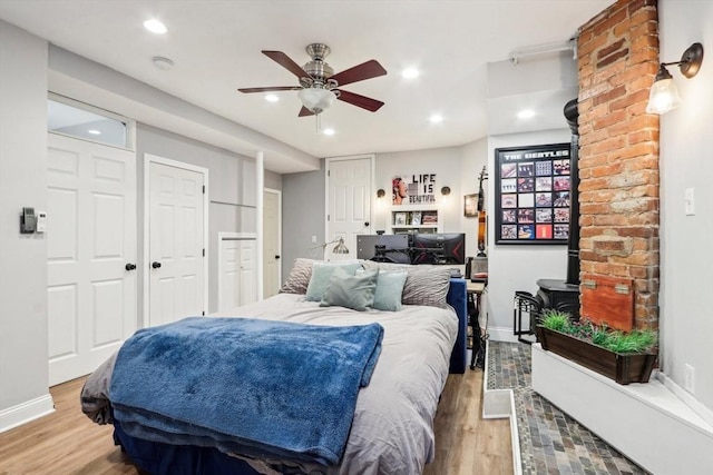 bedroom with ceiling fan, two closets, light hardwood / wood-style floors, and a wood stove