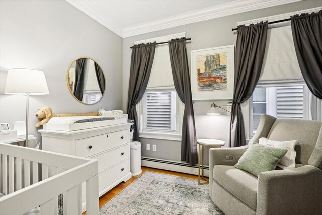 bedroom with a nursery area, crown molding, light wood-type flooring, and a baseboard heating unit