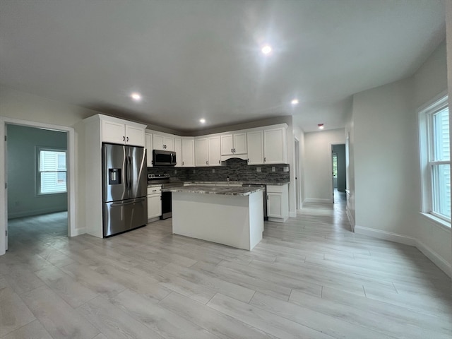 kitchen featuring white cabinets, backsplash, stainless steel appliances, a center island, and dark stone counters