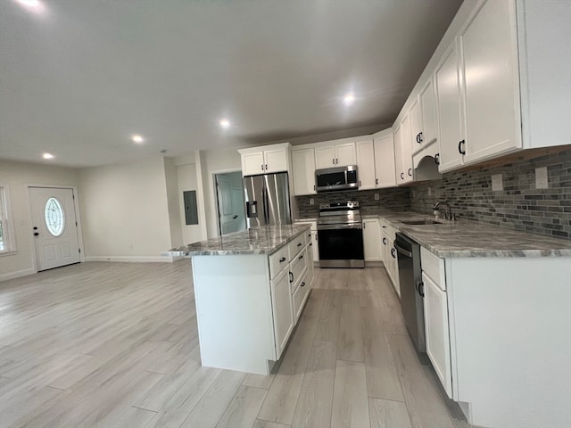 kitchen with light stone counters, white cabinets, a kitchen island, light hardwood / wood-style flooring, and appliances with stainless steel finishes