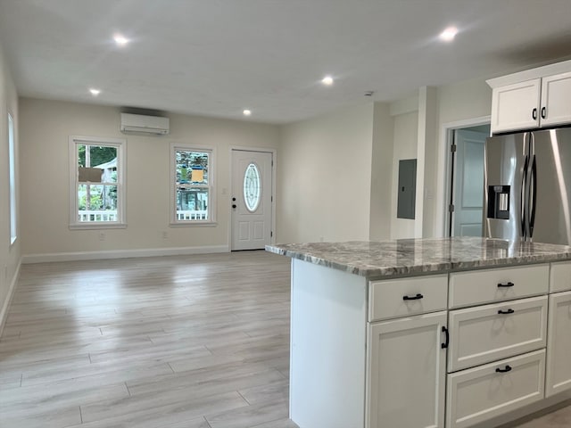 kitchen featuring light stone counters, a wall mounted AC, white cabinetry, stainless steel refrigerator with ice dispenser, and light wood-type flooring