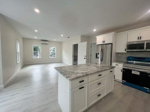 kitchen featuring white cabinetry, light stone counters, a kitchen island, stainless steel appliances, and a wall mounted AC