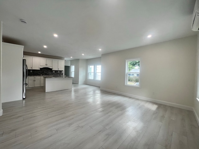 unfurnished living room featuring light hardwood / wood-style floors and a wall mounted air conditioner