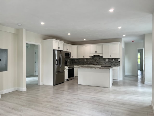 kitchen featuring light hardwood / wood-style floors, white cabinets, a kitchen island, stainless steel appliances, and dark stone counters