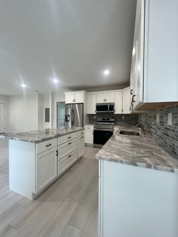 kitchen featuring sink, a kitchen island, white cabinetry, appliances with stainless steel finishes, and light wood-type flooring