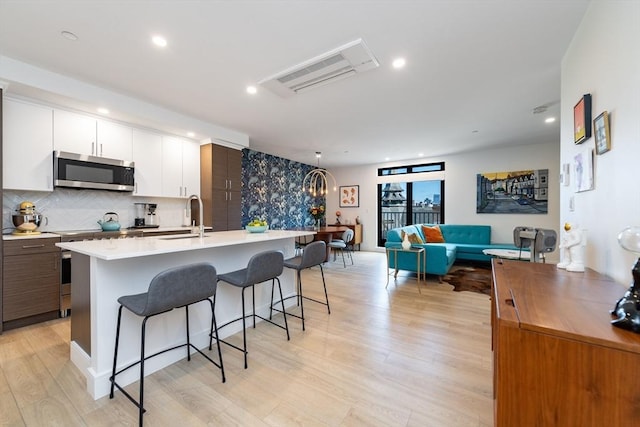 kitchen featuring white cabinets, appliances with stainless steel finishes, an island with sink, sink, and light wood-type flooring