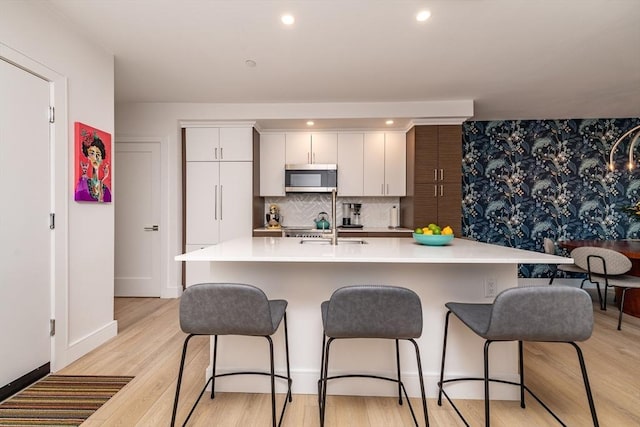 kitchen with light hardwood / wood-style floors, decorative backsplash, white cabinets, a breakfast bar, and sink