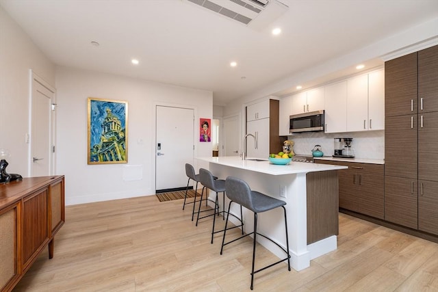 kitchen featuring a kitchen bar, dark brown cabinetry, light hardwood / wood-style flooring, an island with sink, and white cabinets