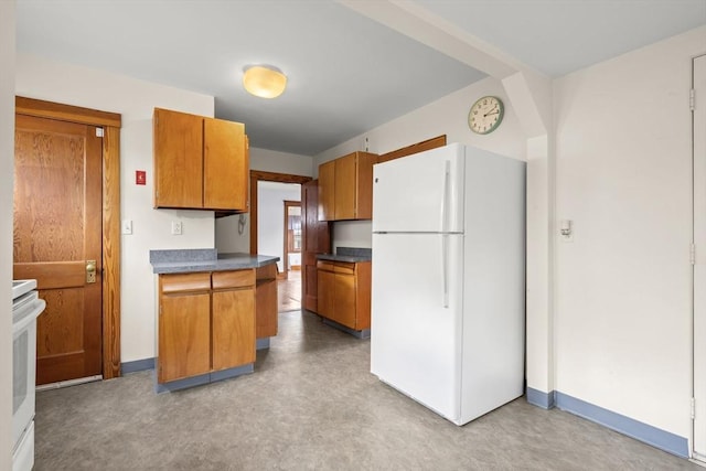 kitchen with brown cabinetry, dark countertops, stove, and freestanding refrigerator