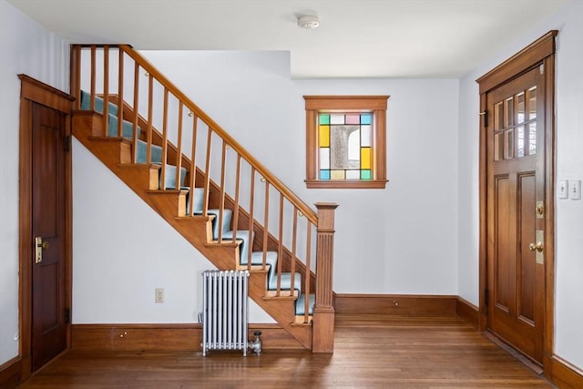 foyer with radiator heating unit, stairs, baseboards, and wood finished floors