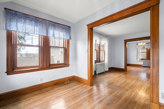 unfurnished room featuring a wealth of natural light, an inviting chandelier, radiator heating unit, and light wood-type flooring