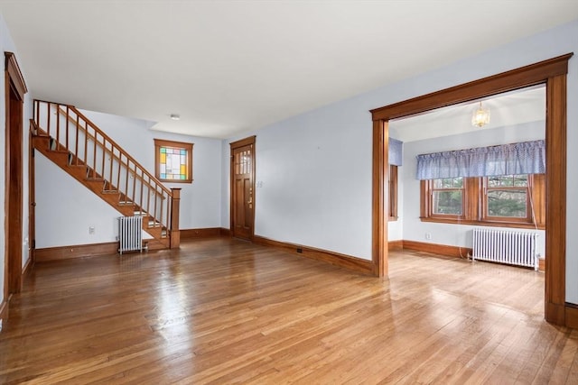 unfurnished living room featuring radiator, a healthy amount of sunlight, baseboards, hardwood / wood-style flooring, and stairs