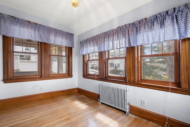 empty room with baseboards, radiator heating unit, lofted ceiling, and light wood-type flooring