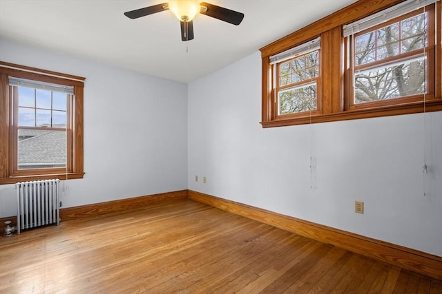 empty room with radiator heating unit, baseboards, light wood-style floors, and a healthy amount of sunlight
