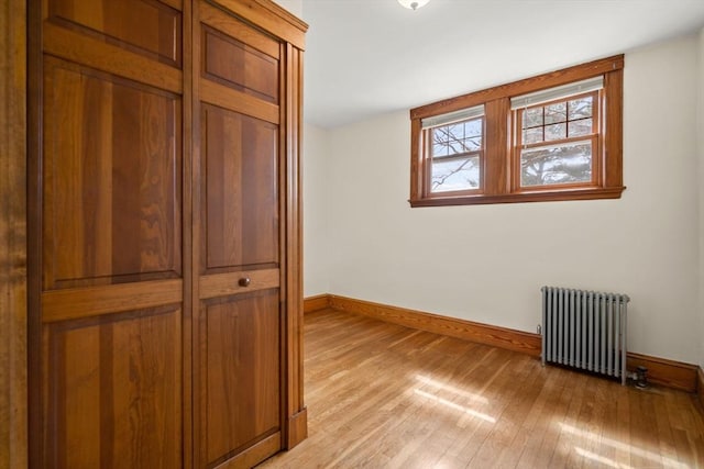 unfurnished bedroom featuring baseboards, radiator heating unit, and light wood-type flooring