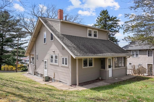 rear view of house with a lawn, a shingled roof, and a chimney