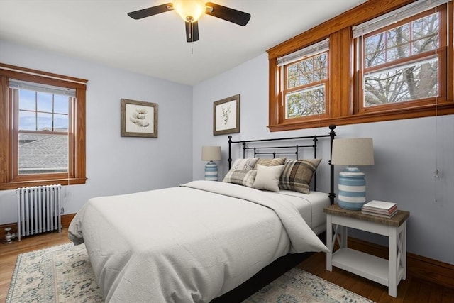 bedroom with radiator heating unit, baseboards, wood finished floors, and multiple windows
