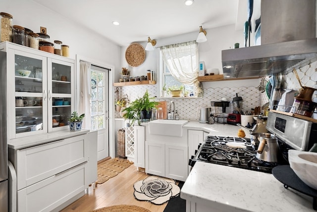 kitchen with white cabinets, sink, tasteful backsplash, light wood-type flooring, and gas range oven