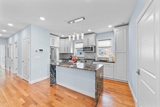 kitchen featuring white cabinets, decorative light fixtures, dark stone countertops, premium appliances, and a kitchen island