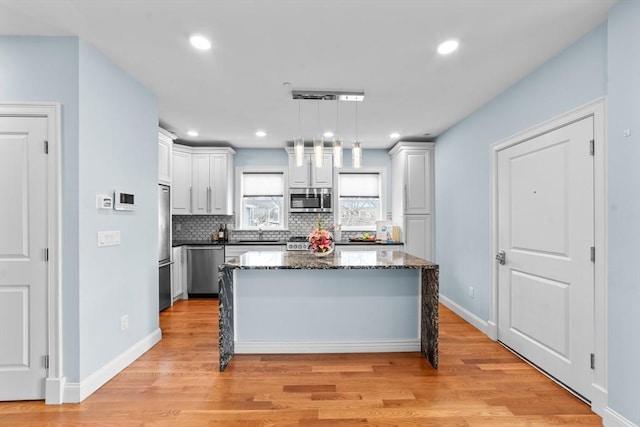 kitchen with dark stone counters, stainless steel appliances, pendant lighting, a center island, and white cabinetry