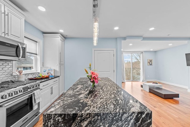 kitchen featuring stainless steel appliances, backsplash, dark stone countertops, white cabinets, and light wood-type flooring