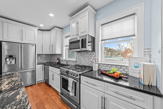 kitchen featuring dark stone counters, stainless steel appliances, sink, light hardwood / wood-style flooring, and white cabinetry