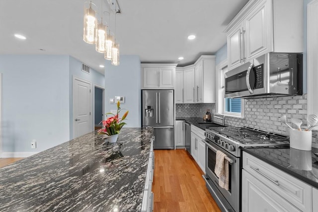 kitchen featuring dark stone counters, white cabinets, sink, decorative light fixtures, and stainless steel appliances