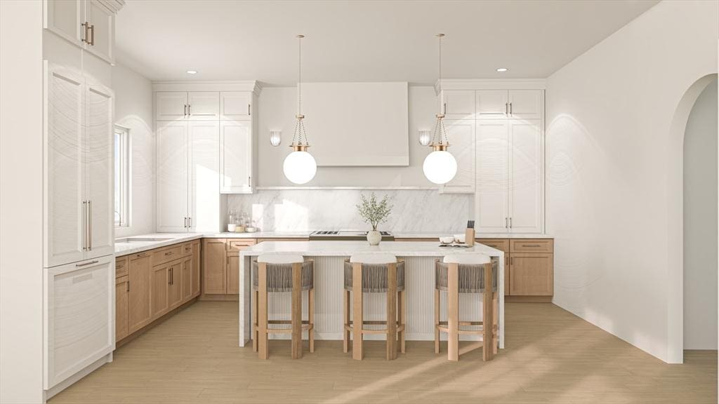 kitchen with light wood-style floors, light countertops, arched walkways, a breakfast bar area, and a center island