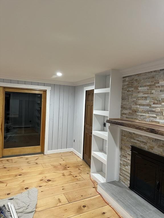 unfurnished living room with ornamental molding, a stone fireplace, and light hardwood / wood-style flooring