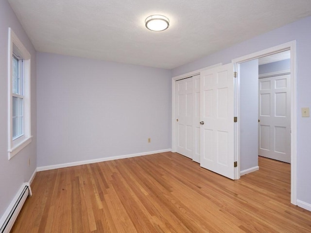 unfurnished bedroom with light hardwood / wood-style flooring, a closet, and baseboard heating