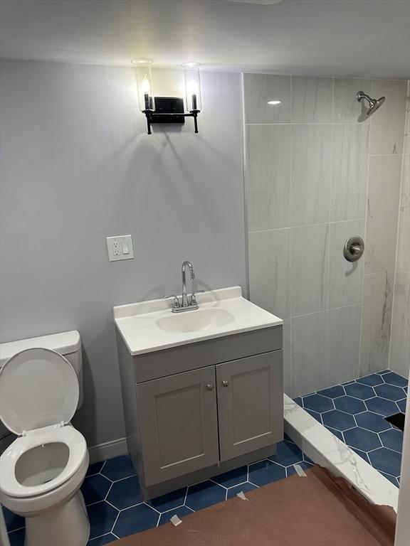 bathroom featuring vanity, tile patterned flooring, toilet, and tiled shower