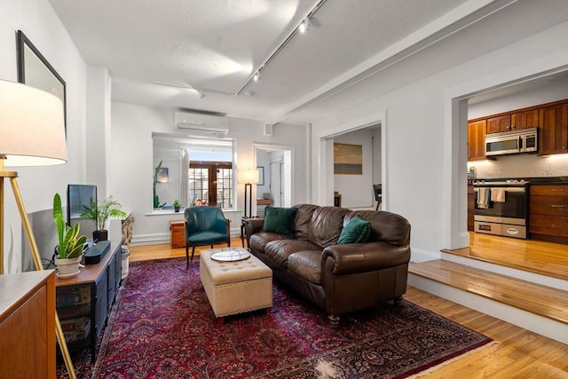 living room with a wall mounted air conditioner, light wood-style flooring, and rail lighting